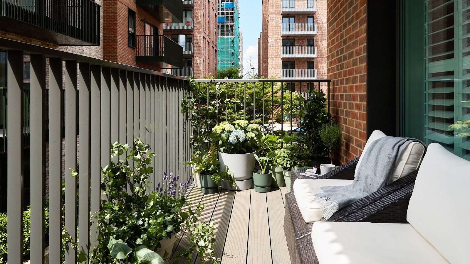 A sunny urban balcony, decorated with potted plants and two wicker armchairs.